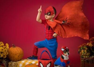 A boy in a spiderman costume with a dog on a red background.