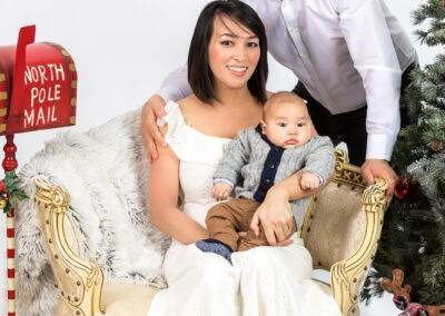 A man and woman pose with a baby in front of a christmas tree.