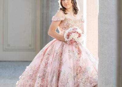 A young woman in a pink dress is posing in front of pillars.