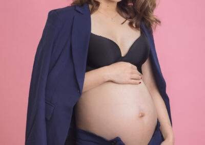 A pregnant woman in a suit posing on a pink background.