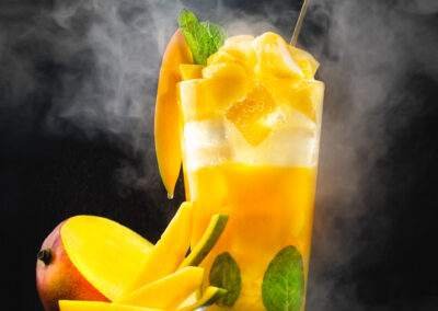 A mango cocktail with ice and smoke on a black background.