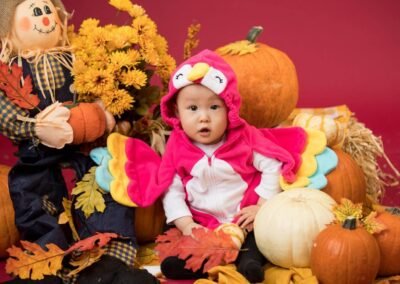 A baby dressed as an owl in front of pumpkins and scarecrows.