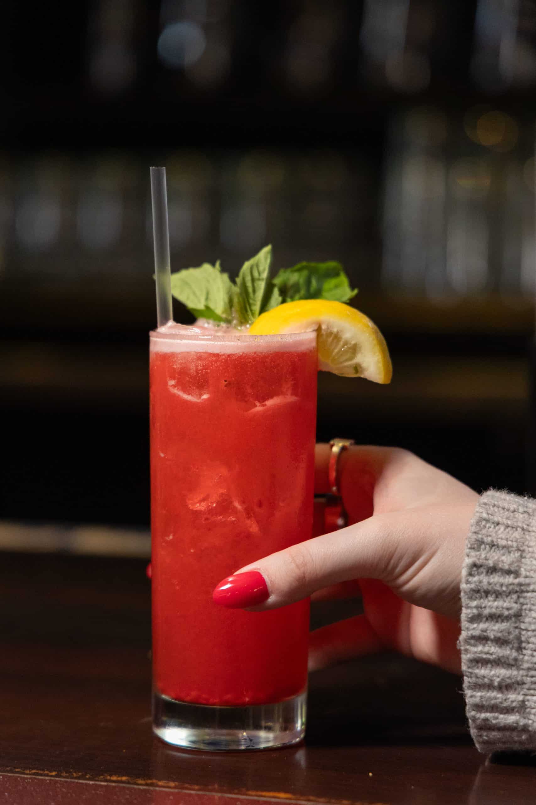 Red cocktail with basil and lemon garnish at The Comedy Bar