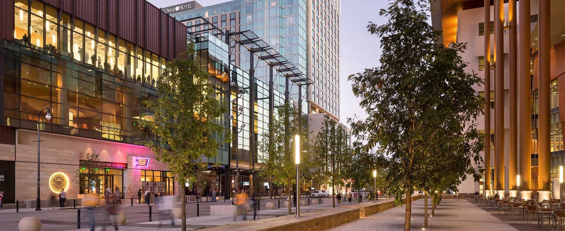 Modern urban street with trees, shops, and office buildings at dusk.