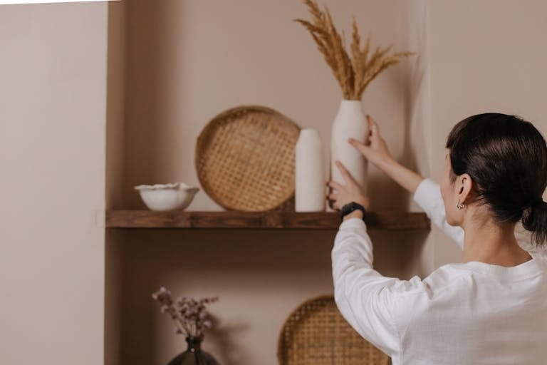 A woman arranging vases on a rustic shelf, highlighting minimalist interior design.