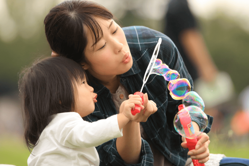 A young girl and adult blowing bubbles outdoors, promoting healthy activities for children to prevent substance abuse.