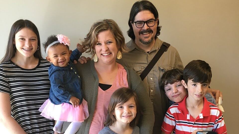 A diverse family group smiling and embracing, representing love and support in foster, adoption, and kinship care.