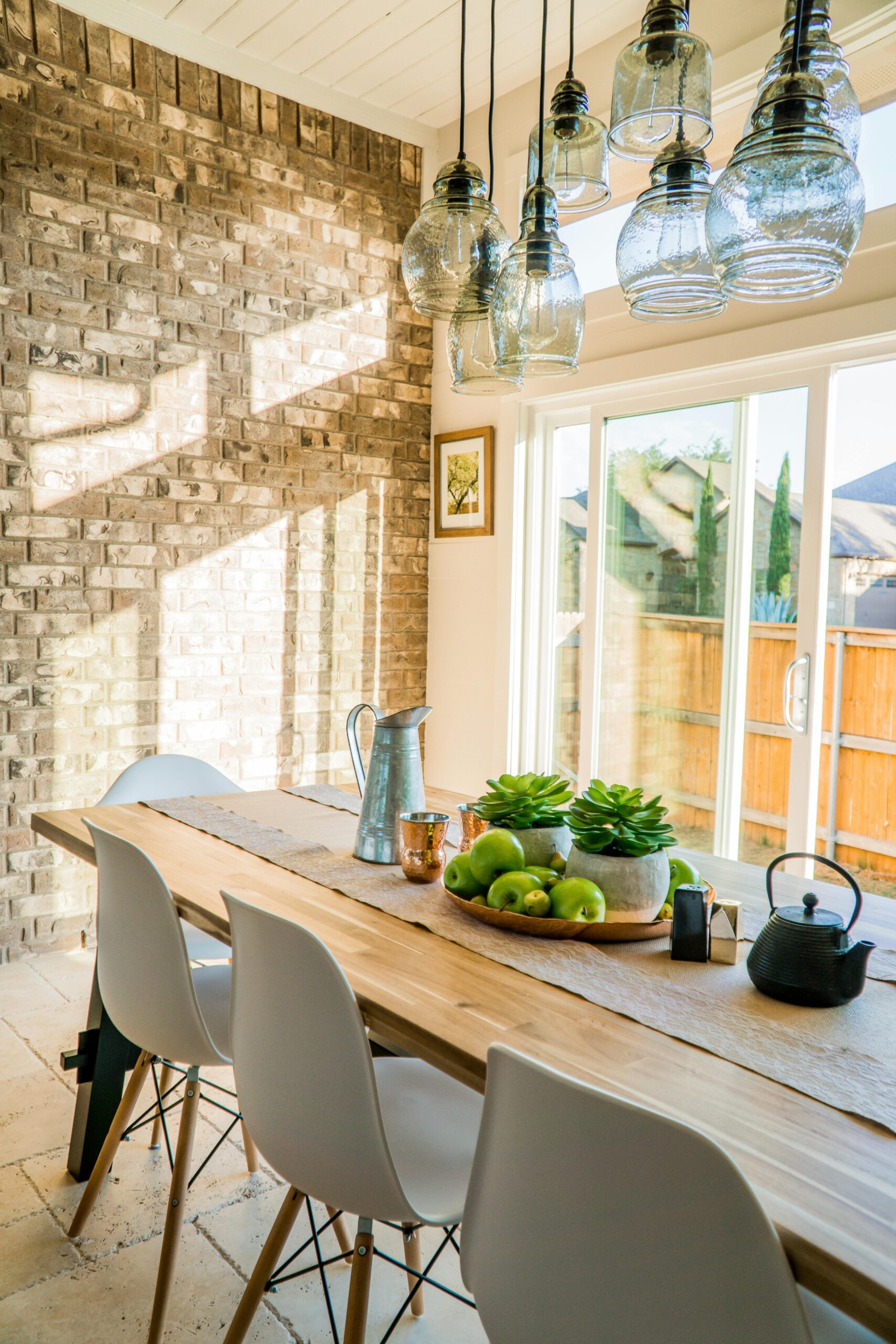 Dining room with a long wooden table, white chairs, and glass pendant lights.