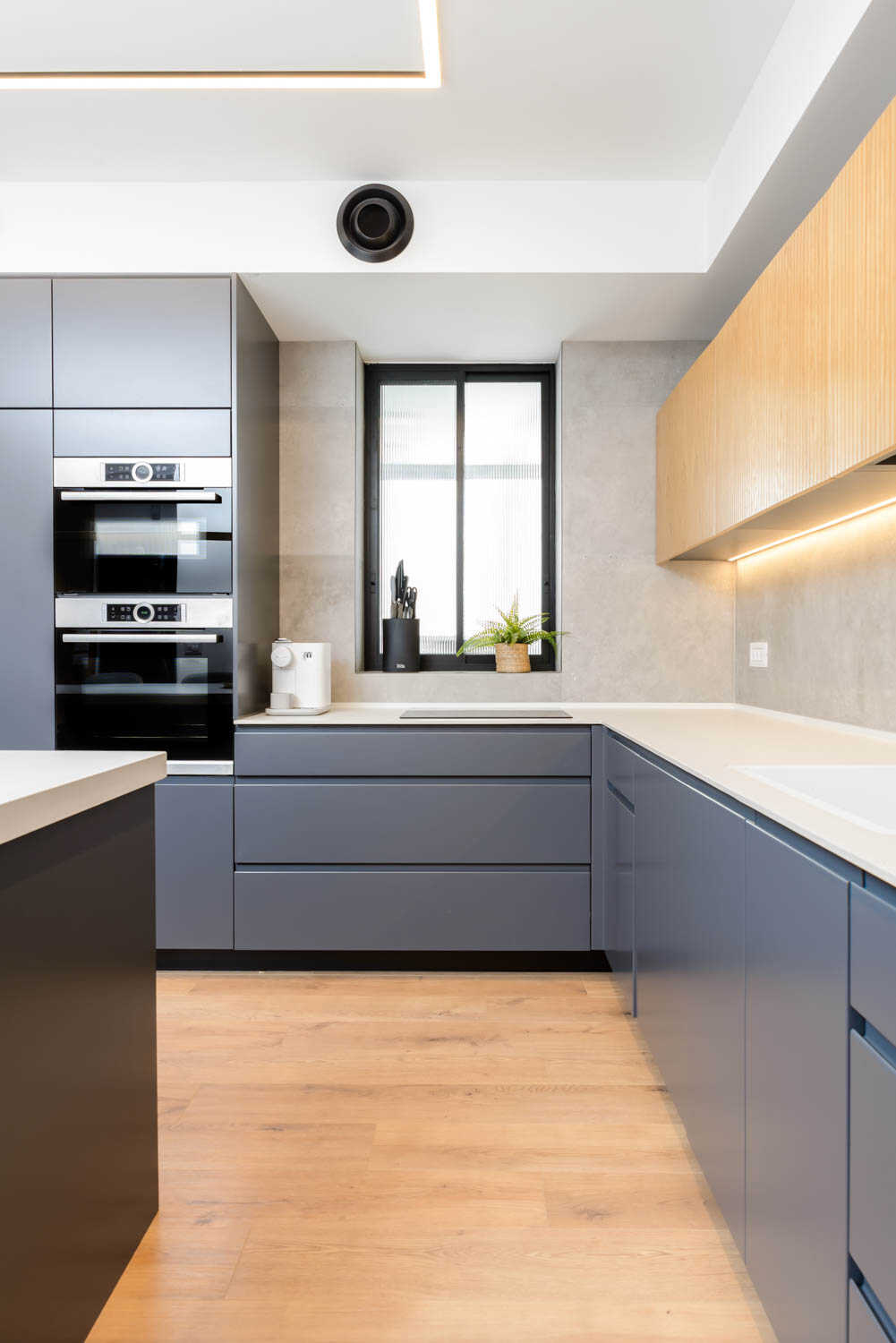 Modern kitchen with gray cabinets, wood accents, and built-in ovens.