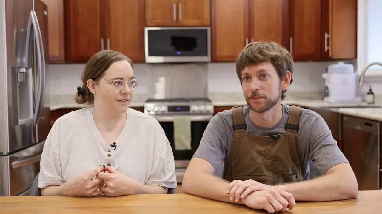 Two people sitting at a table in a kitchen, looking forward