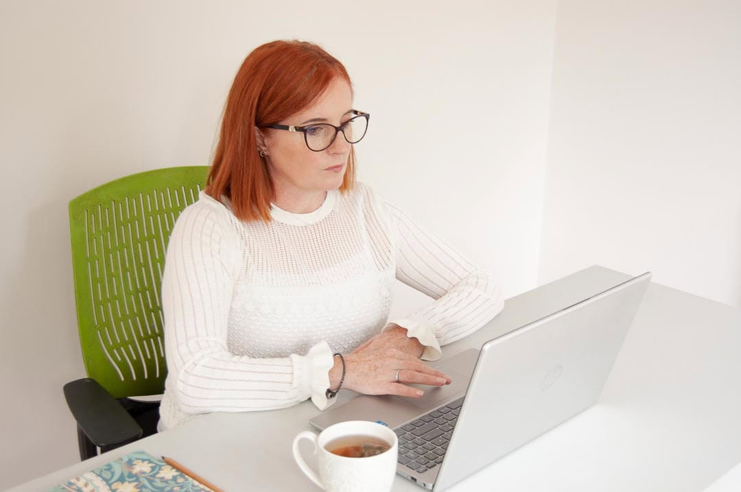 Deirdre Egan, midlife nutritionist, working on her laptop with a cup of tea, delivering online wellbeing support for corporate clients