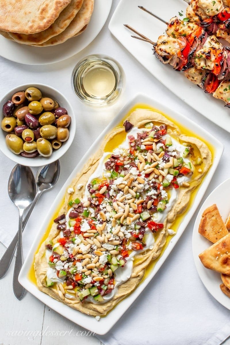Greek layered hummus dip topped with yogurt, veggies, olives, and herbs.