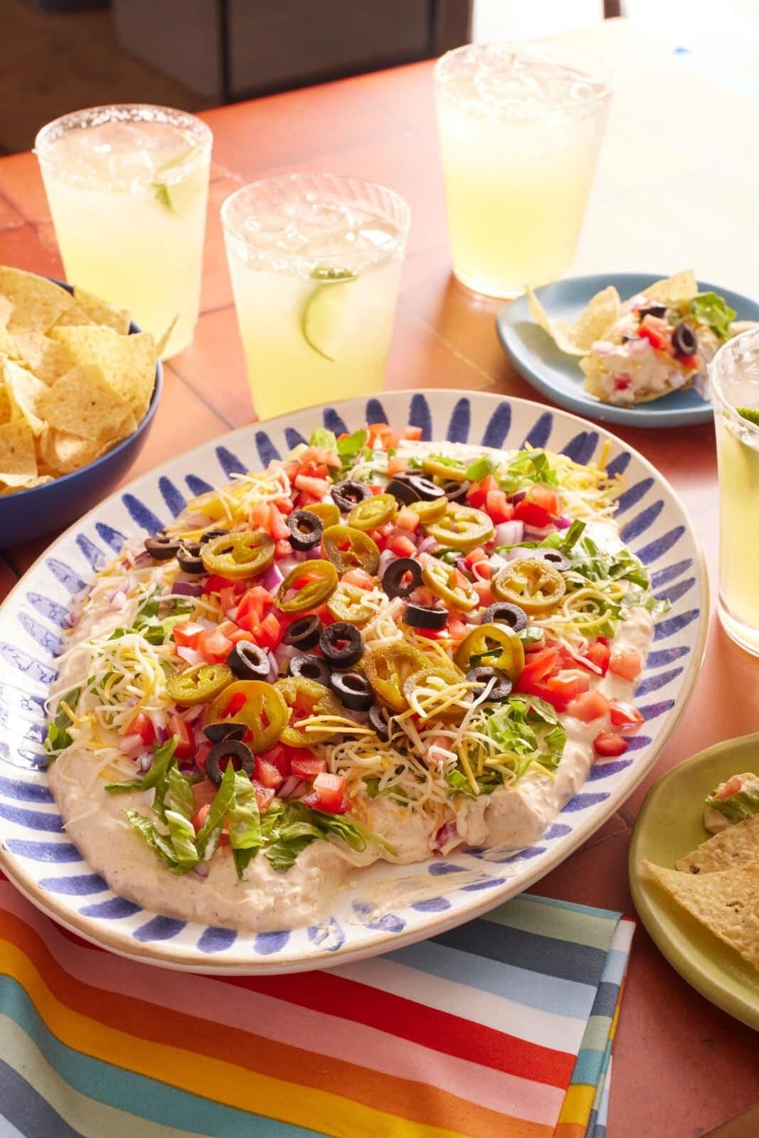 Layered taco dip topped with cheese, olives, and tomatoes.
