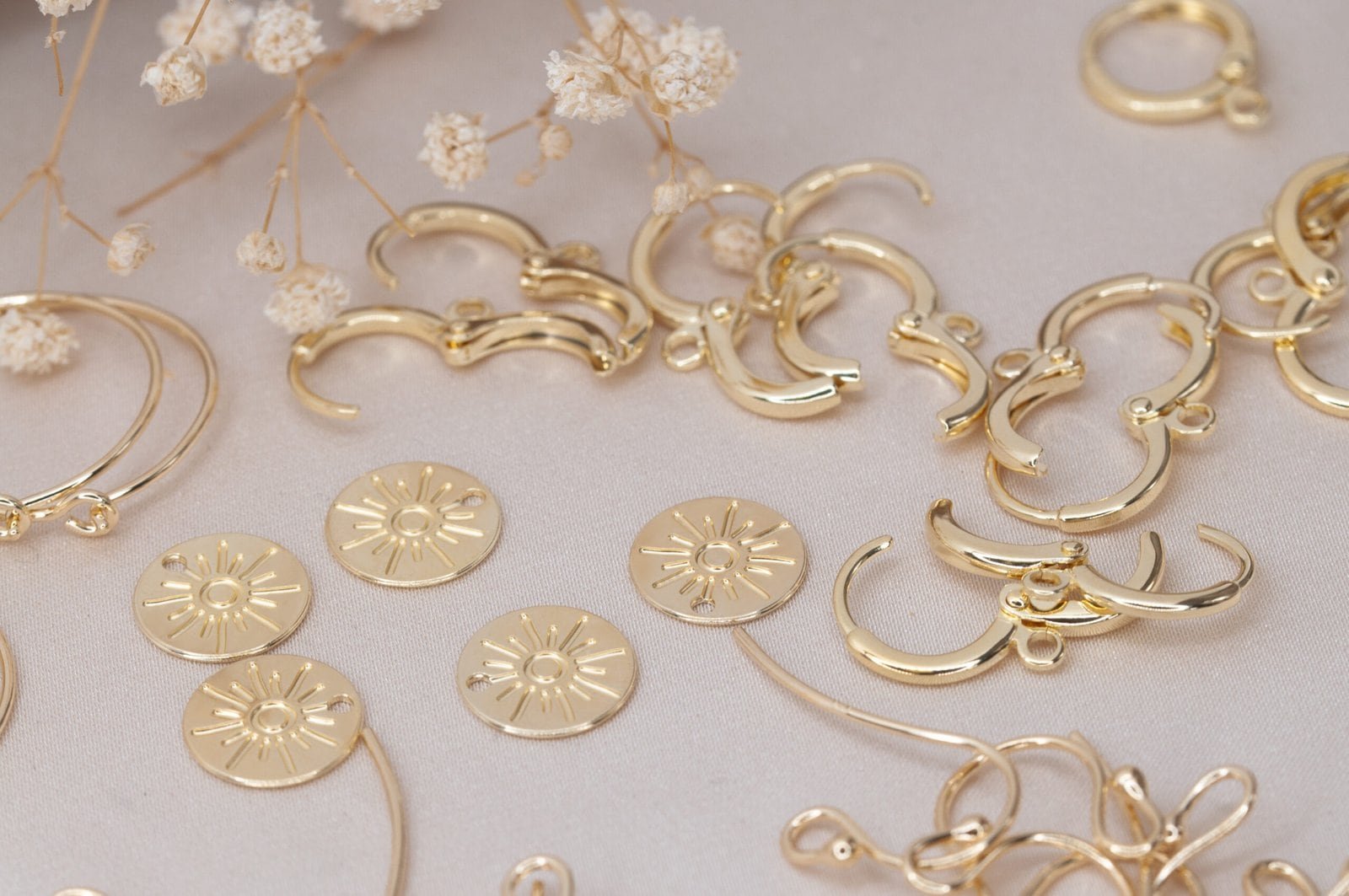 Gold sun disc charms, hoops, hooks and leverback bases laid out as components for different earring styles