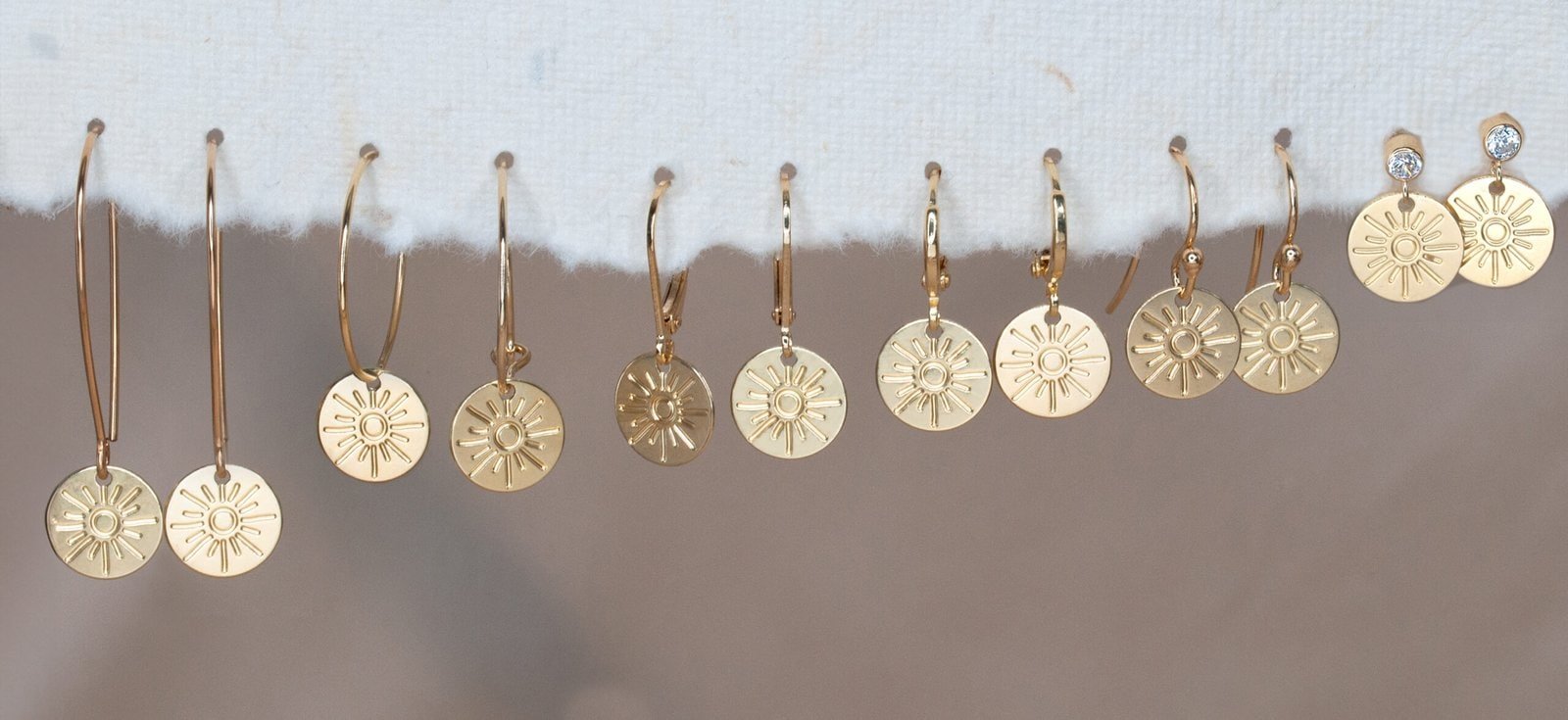 Gold sun disc earrings styled flatlay with dried flowers and soft textured fabrics