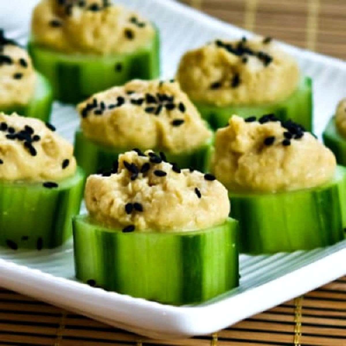 Cucumber hummus bites topped with sesame seeds on a white platter.