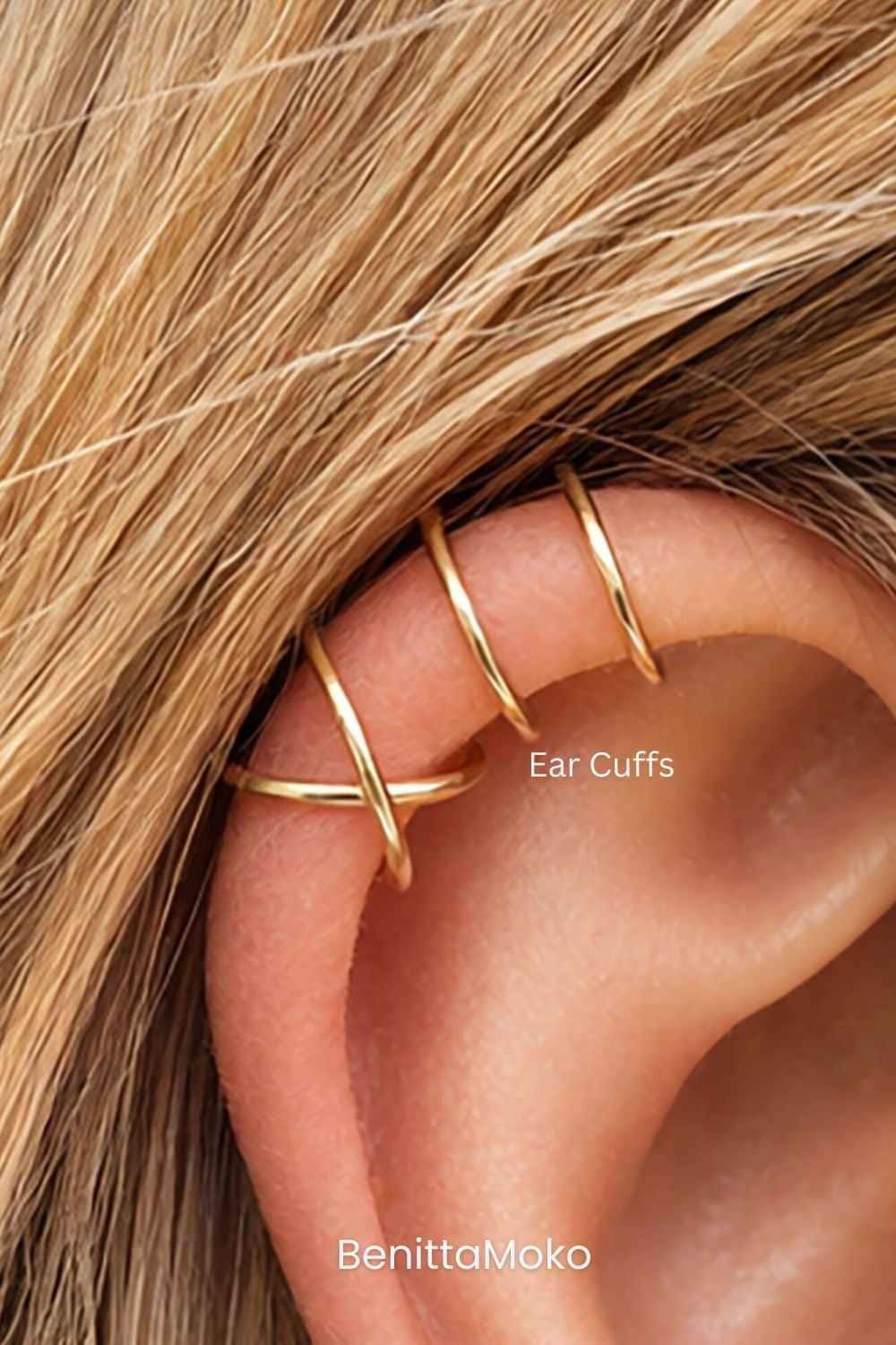 Gold ear cuffs styled on upper ear cartilage, close-up of minimalist helix cuff jewelry in warm natural tones