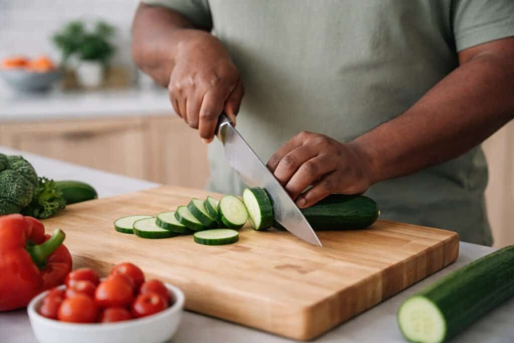 Person slicing vegetables on a stable cutting board with proper knife technique