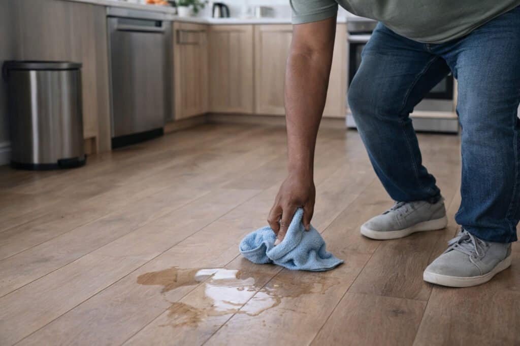 Person wiping a kitchen floor spill to prevent accidents