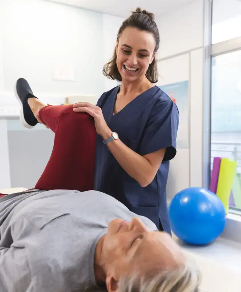 Female physiotherapist assisting patient with leg exercise in clinic.