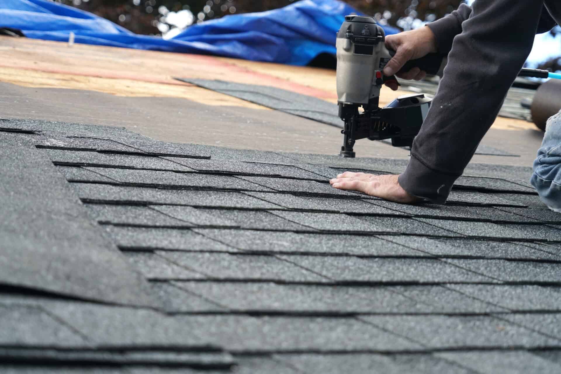 handyman using nail gun to install shingle to repair roof