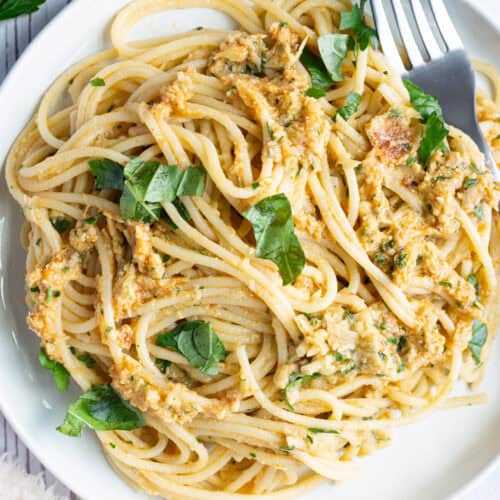 A plate of artichoke and sun-dried tomato pasta garnished with fresh basil.