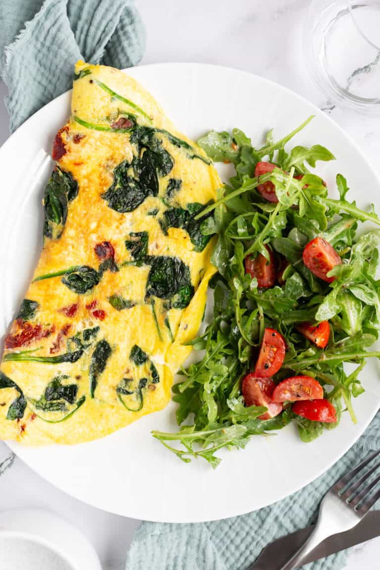 A sun-dried tomato omelette served on a white plate with a side salad.