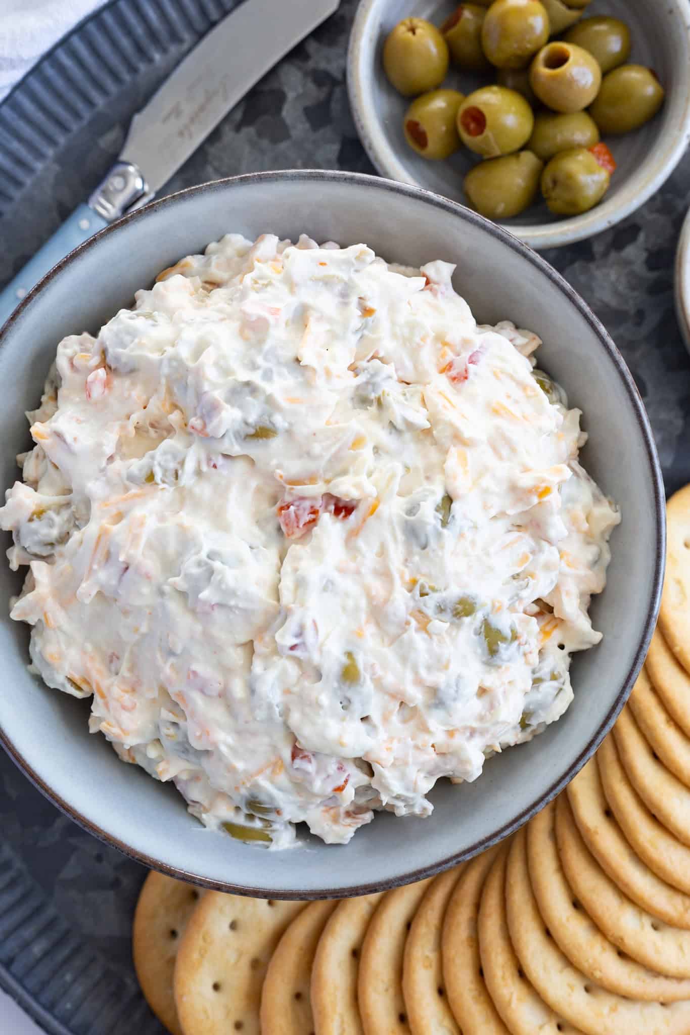 Olive dip with almonds on a platter filled with crackers and a small bowl of green olives.
