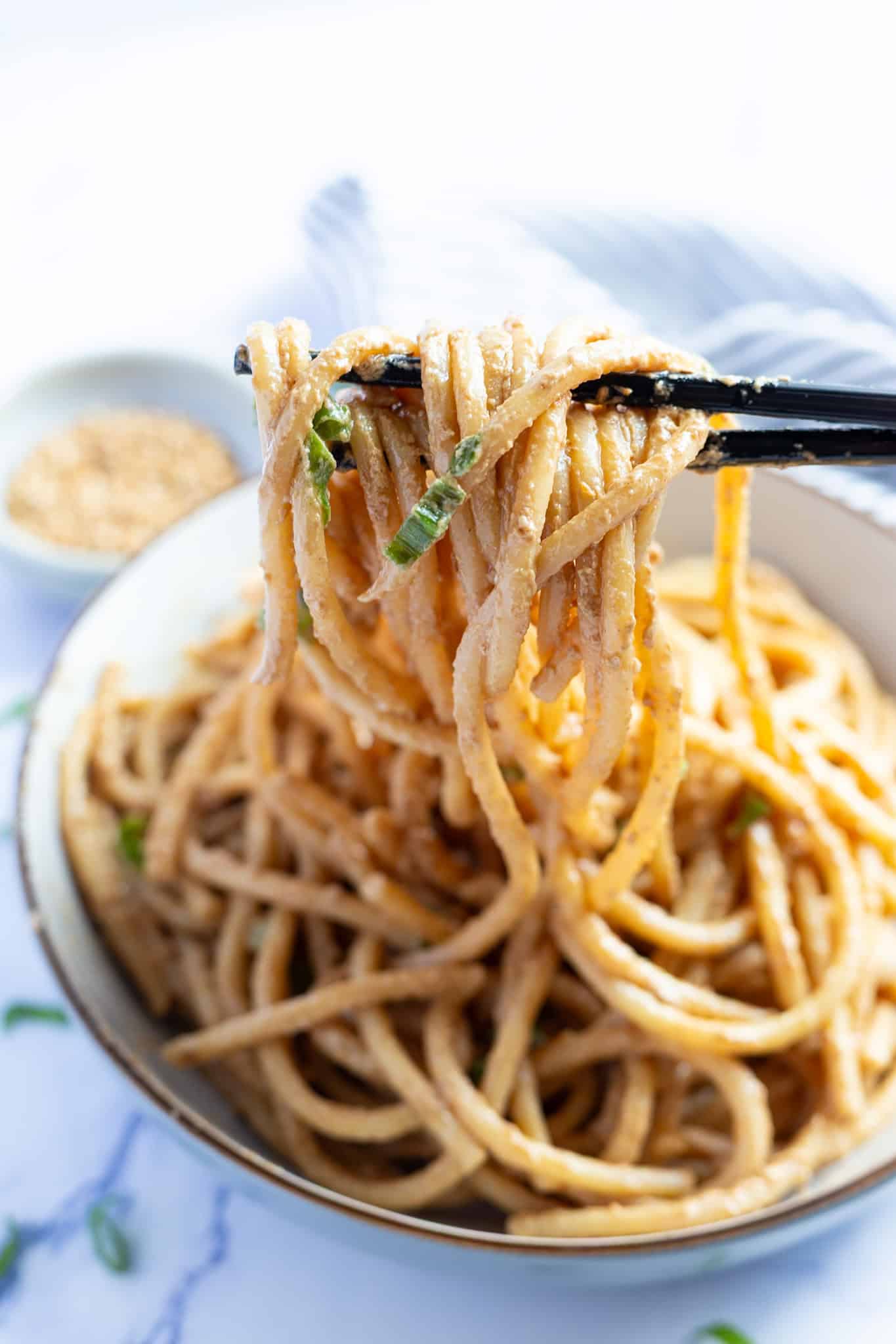 Strands of cold sesame noodles twisted around a pair of chopsticks.