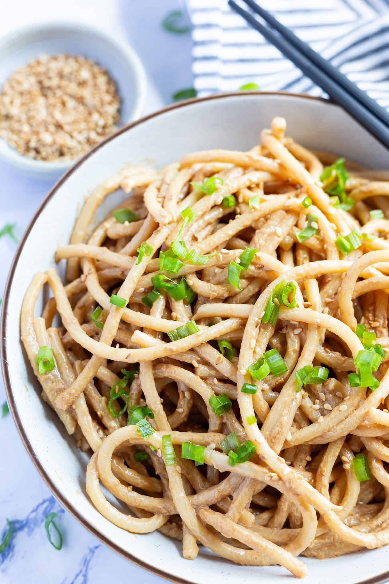 A bowl of cold sesame noodles garnished with scallions.