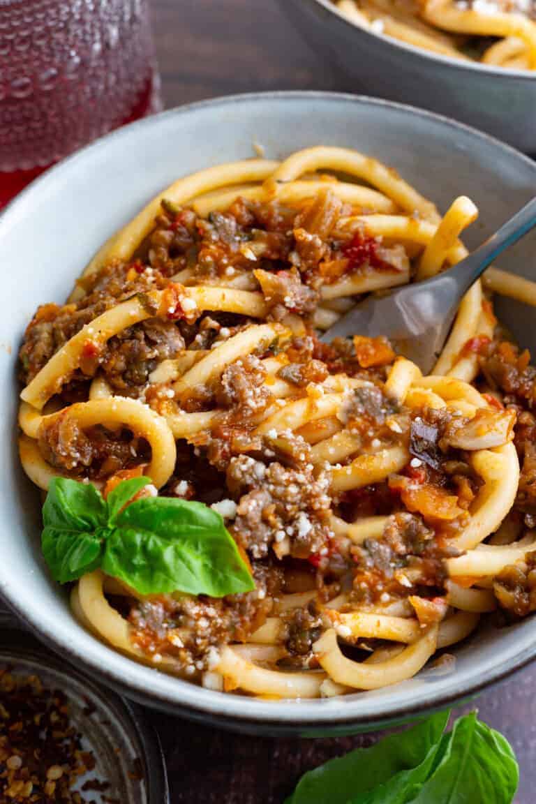 A bowl of bucatini bolognese with veggies and sausage.