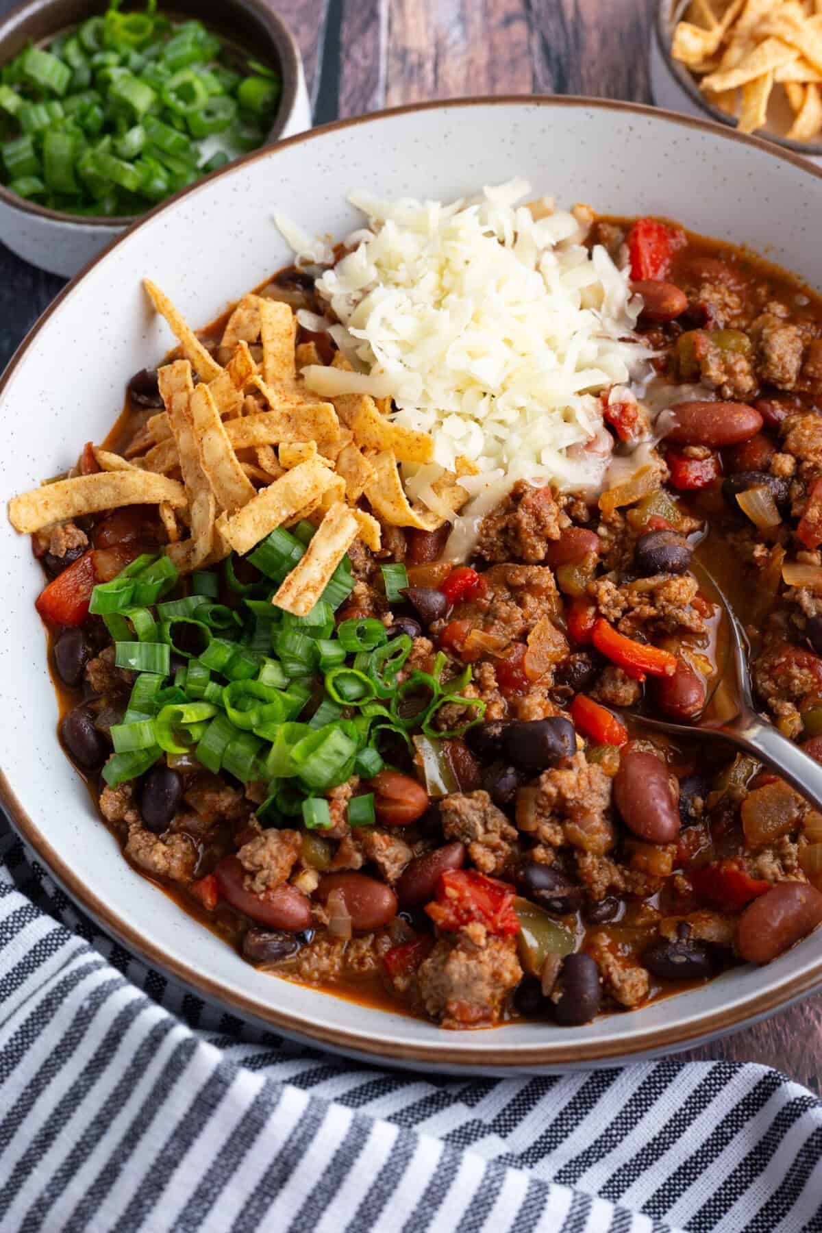 A bowl of turkey chili topped with scallions, shredded cheese, and tortilla strips.