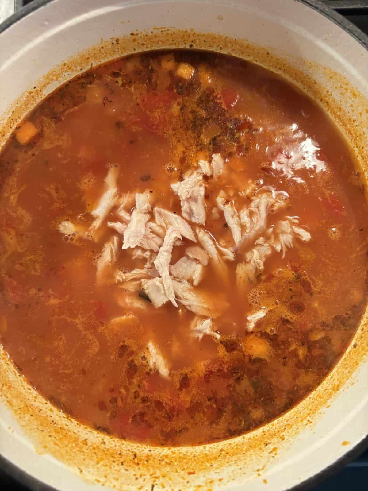A pot of turkey orzo soup with the turkey added.