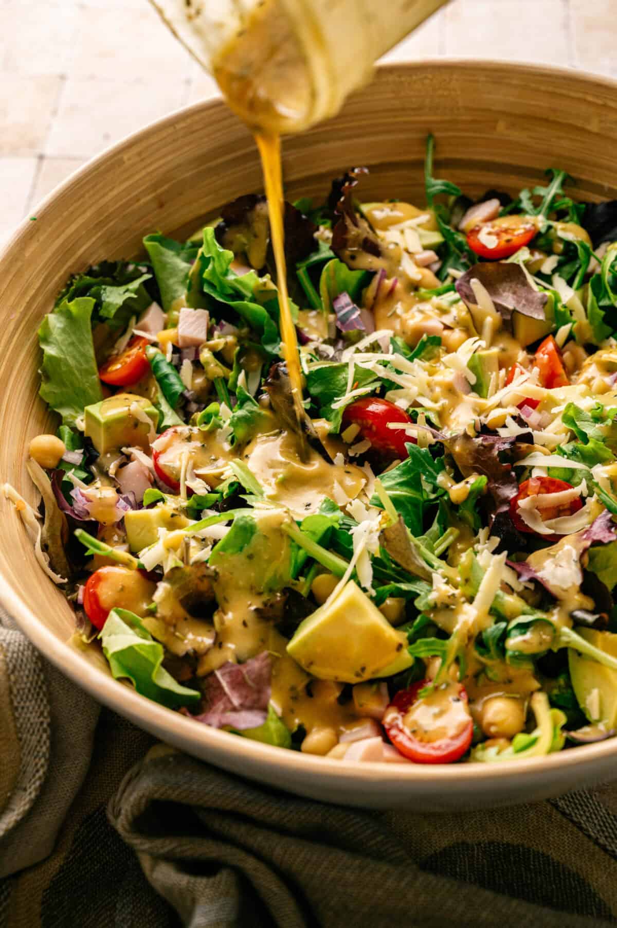 A bowl of salad with smoked turkey with dressing being poured.