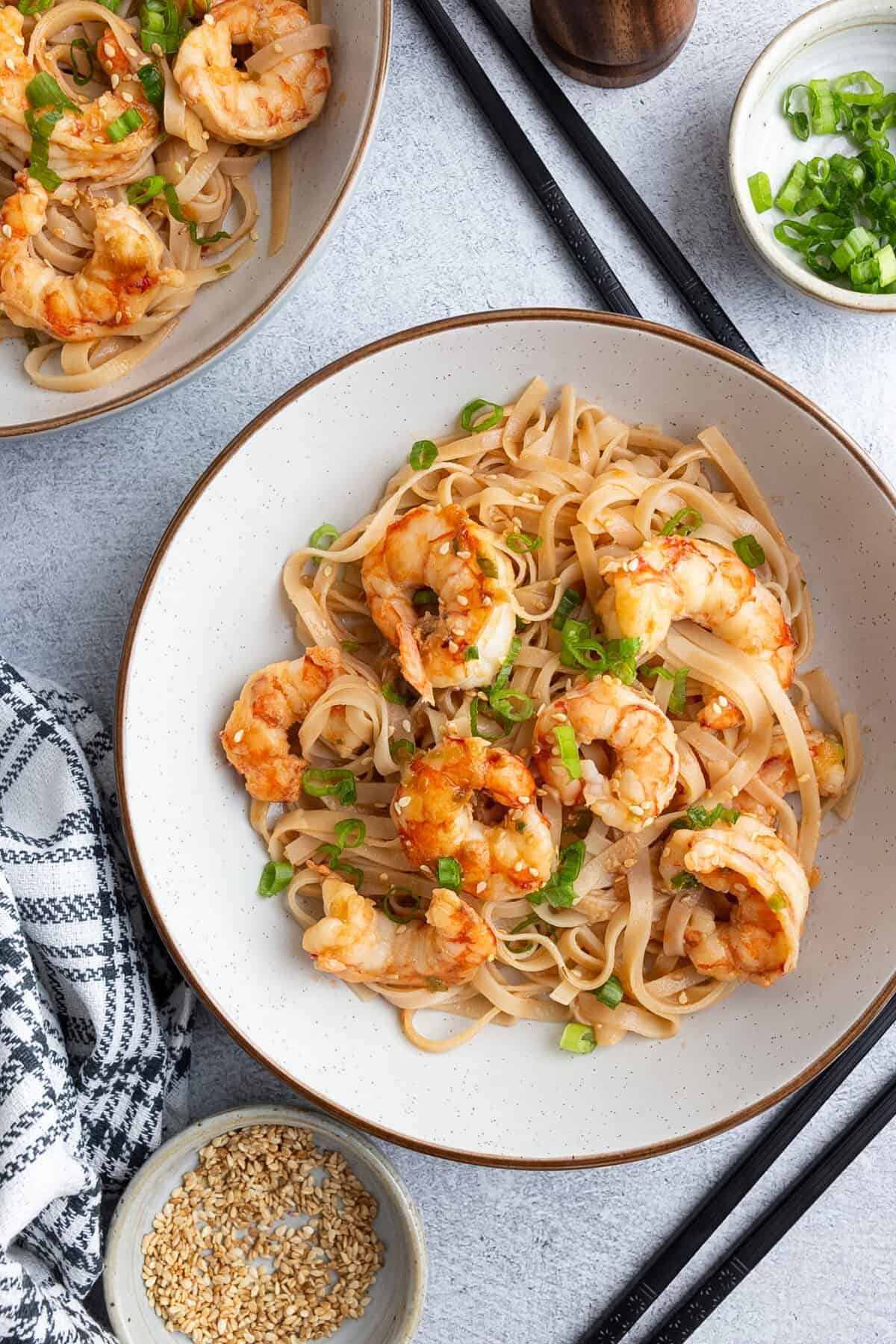 A bowl of rice noodles tossed with shrimp and garnished with scallions.