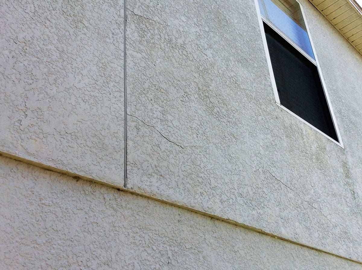 Cracked stucco wall with a window and a roofline visible