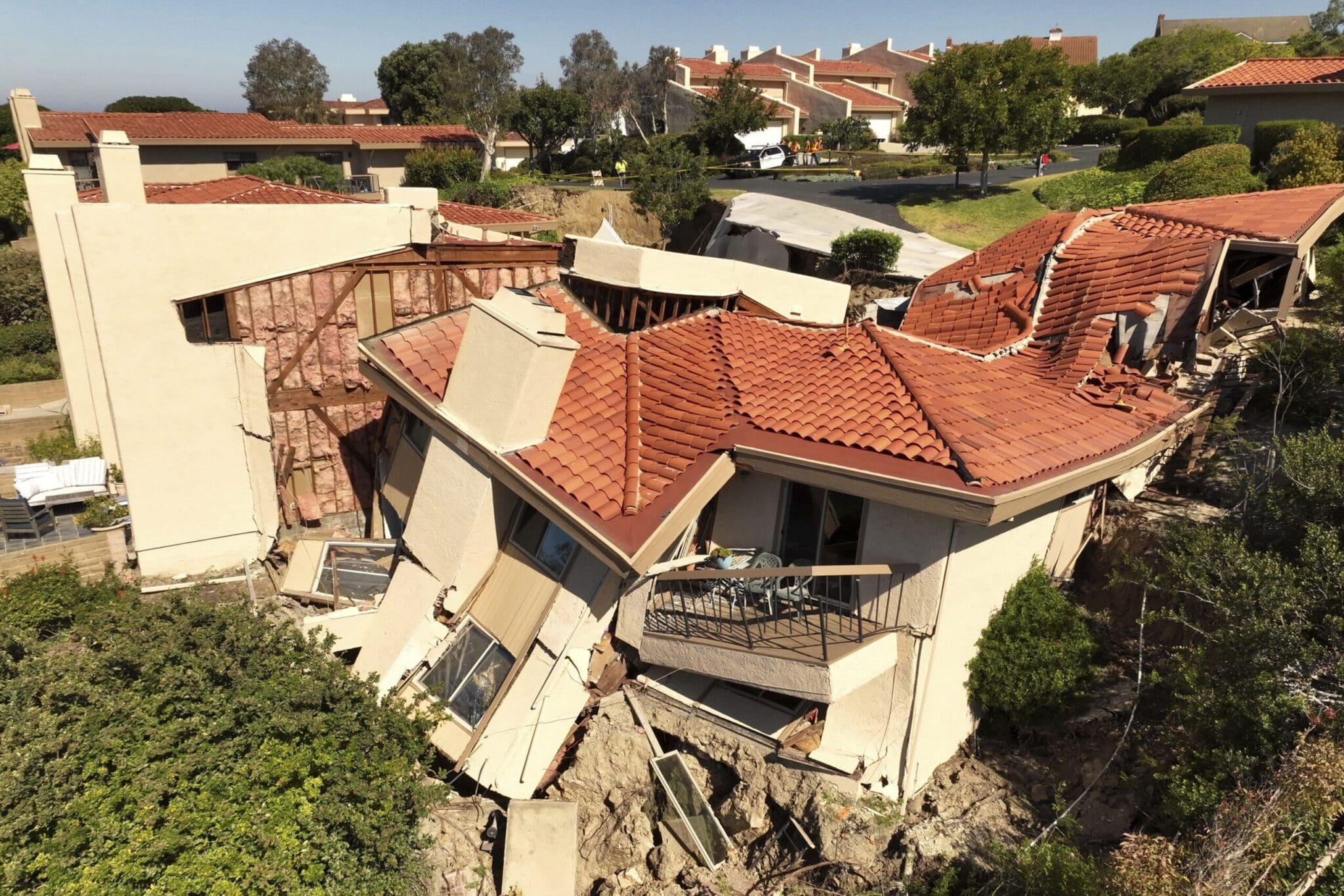 Houses damaged by a landslide, with roofs collapsed and structures tilted.