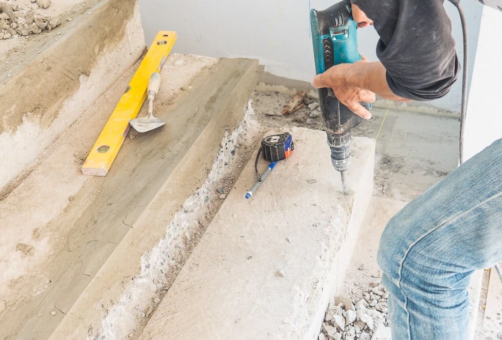 Person drilling into concrete steps during construction with tools nearby