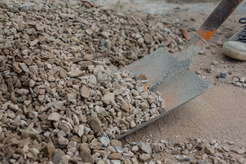 Close-up of a shovel scooping gravel from a pile on the ground.