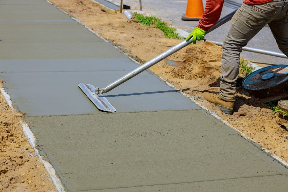 Worker smoothing wet concrete for a new sidewalk