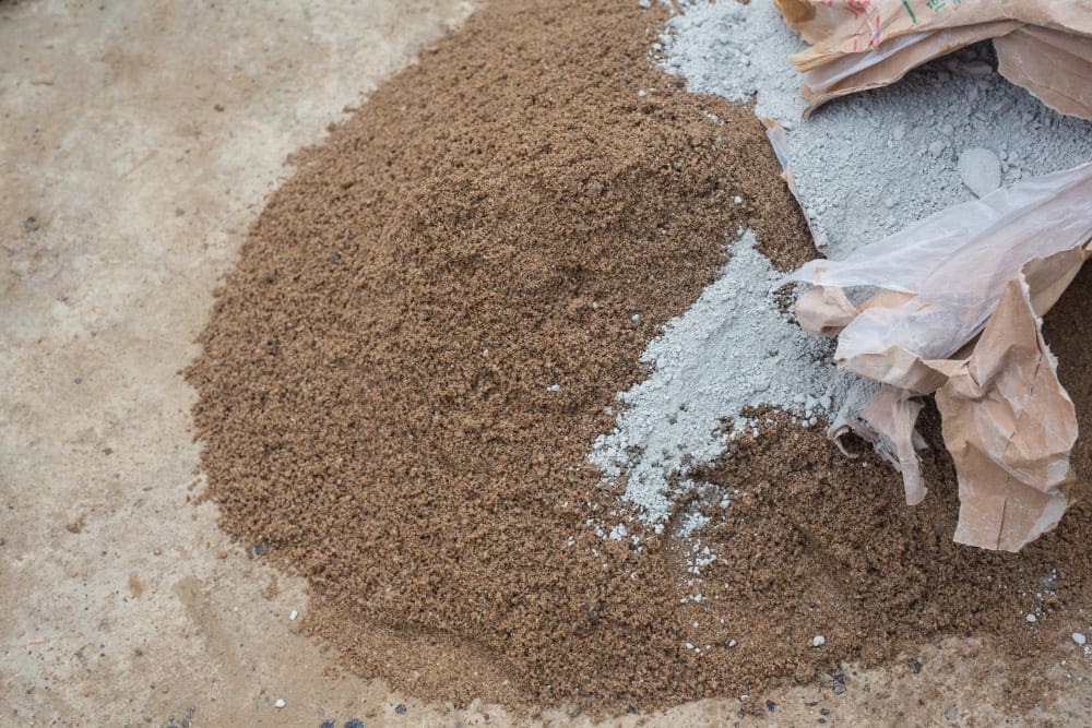 Pile of brown sand and gray cement powder on concrete.