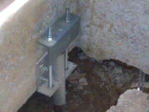 Metal bracket with bolts securing a foundation in a dug-out area