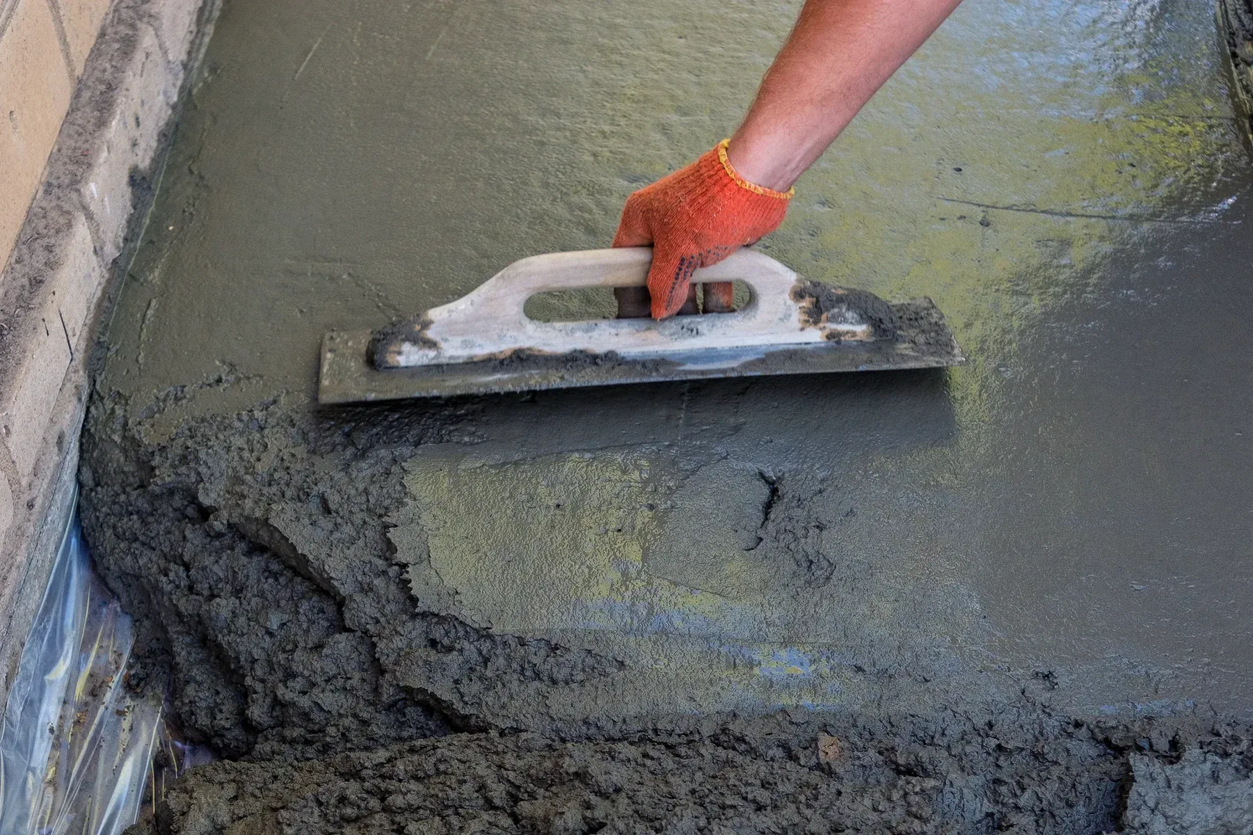 Hand in orange glove smoothing wet concrete with a trowel