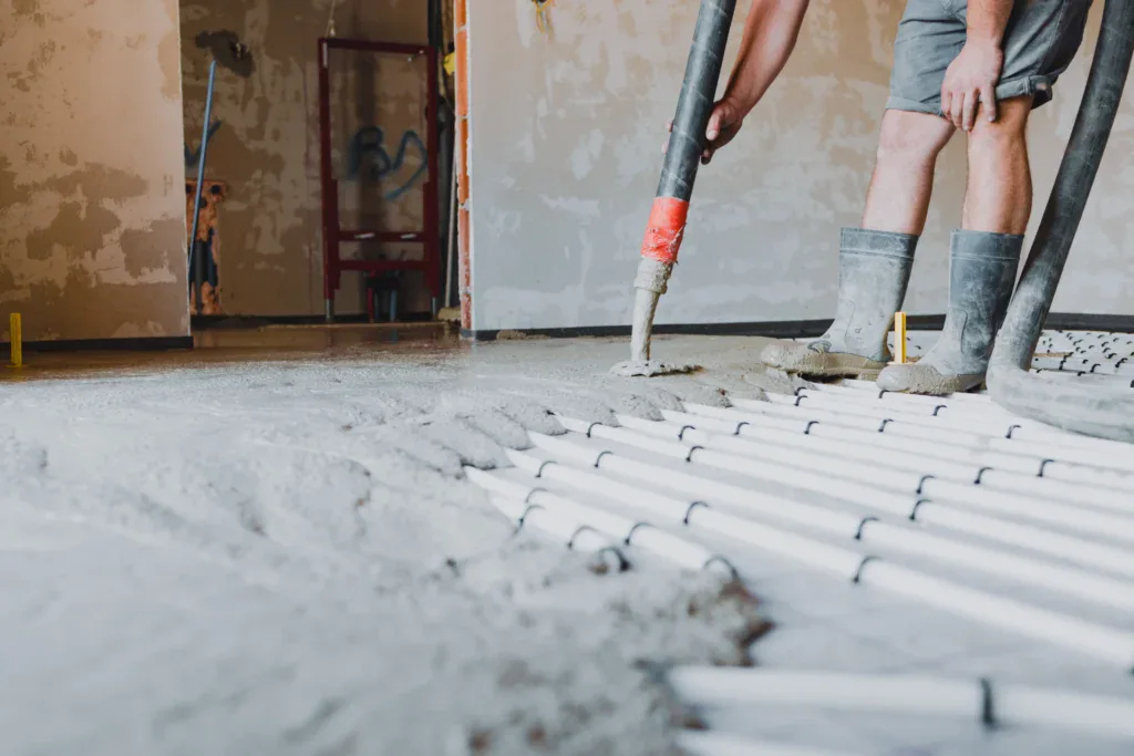 Worker pouring concrete over underfloor heating pipes during construction