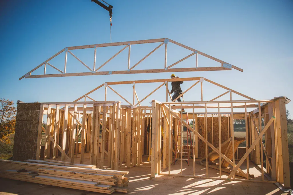 Construction worker guiding a roof truss onto a house frame