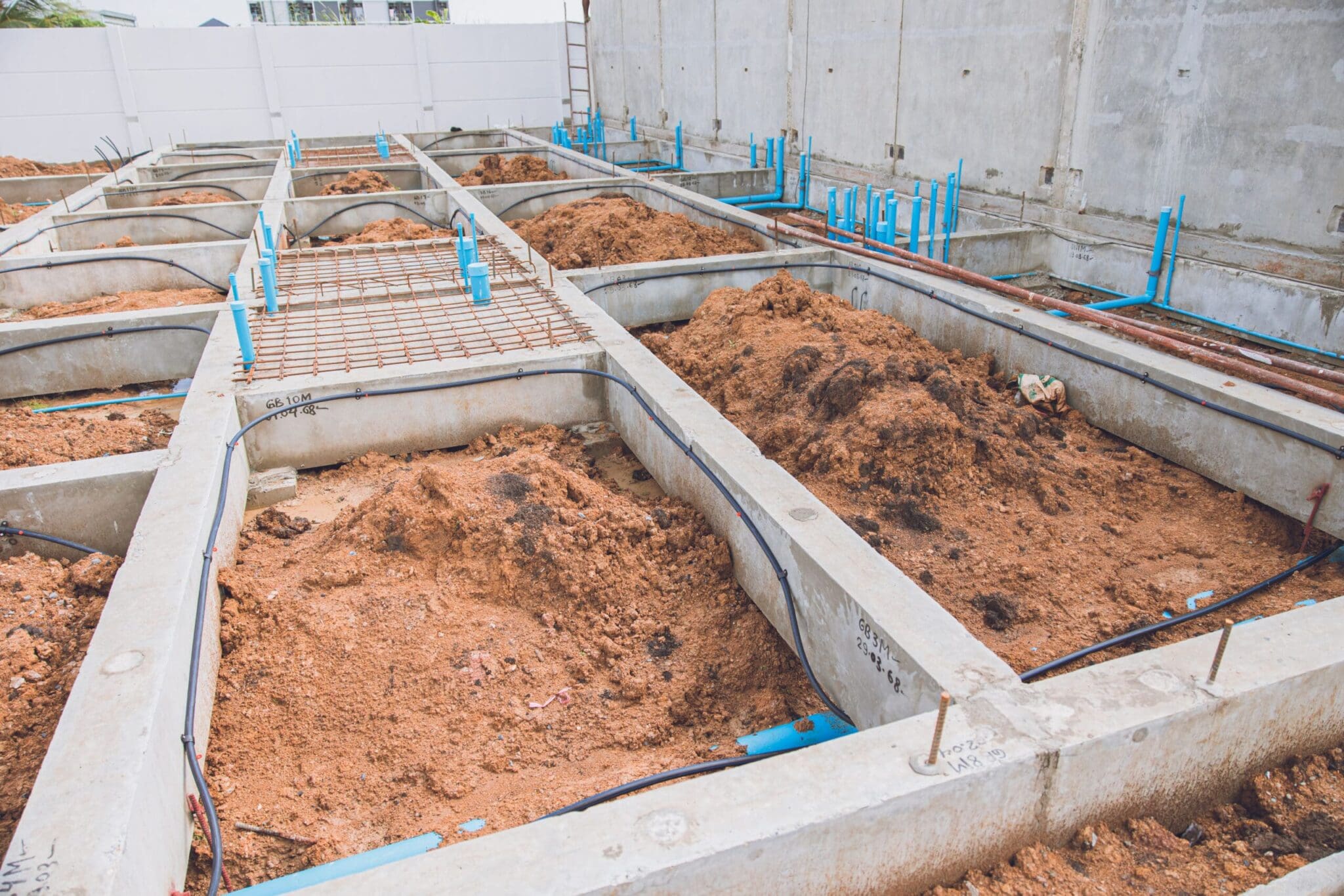 Construction site with concrete foundations, soil, and blue pipes
