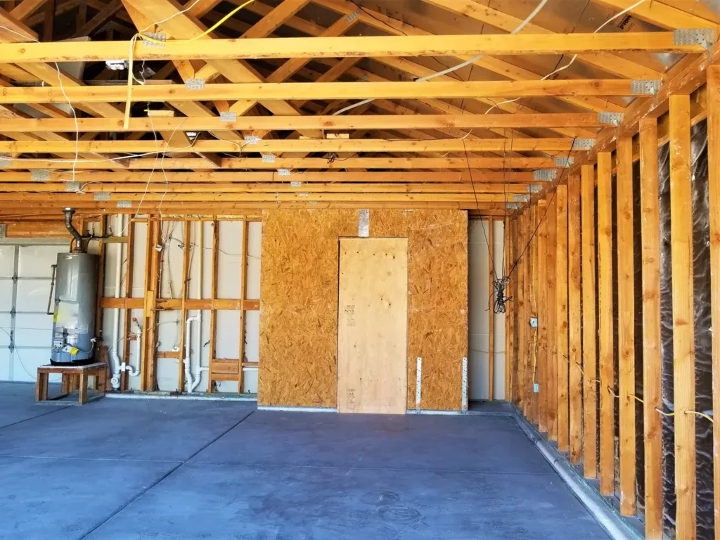 Unfinished garage interior with exposed wooden framing and water heater