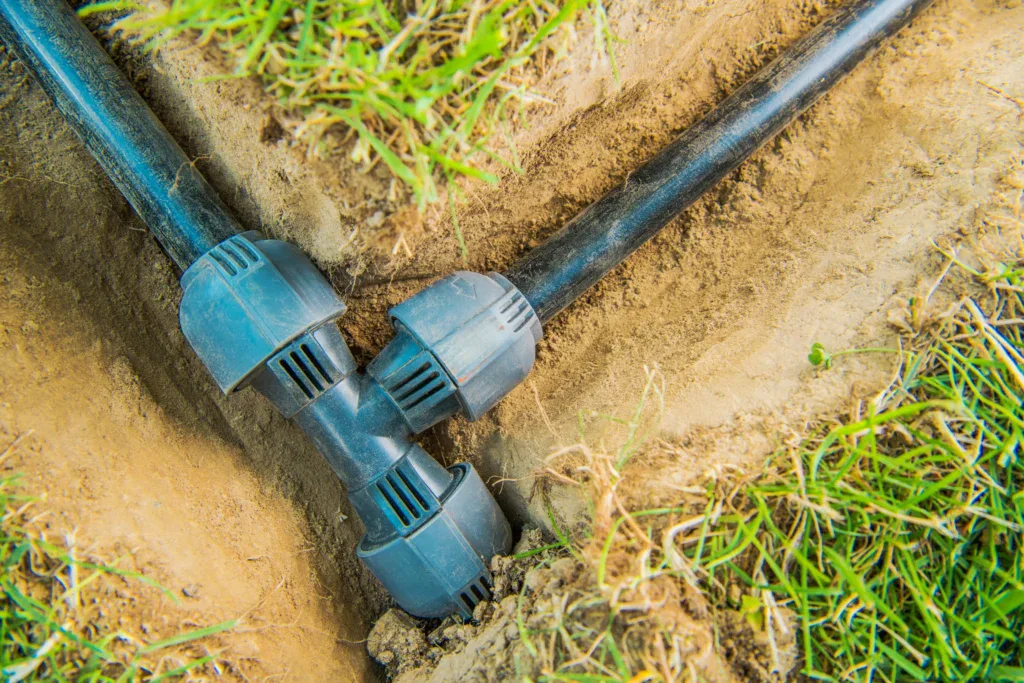 Black irrigation pipes connected by a T-joint in a trench.
