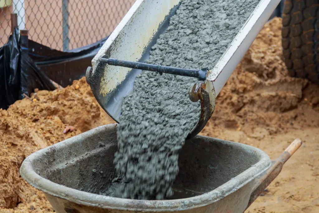 Wet concrete pouring from a chute into a wheelbarrow at a construction site.