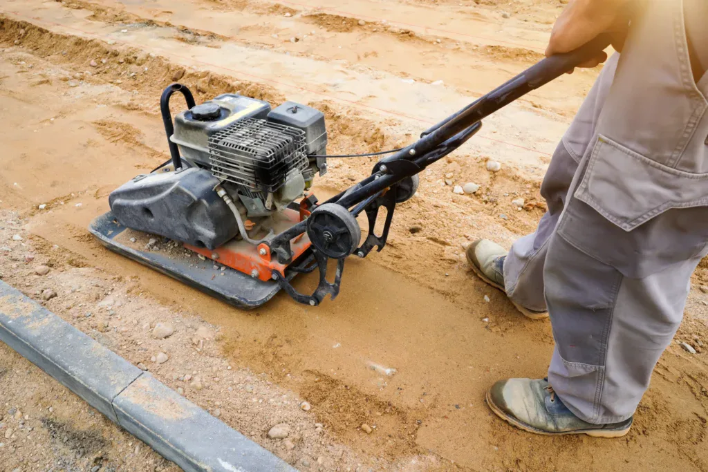 Worker compacting sand with a plate compactor on a construction site